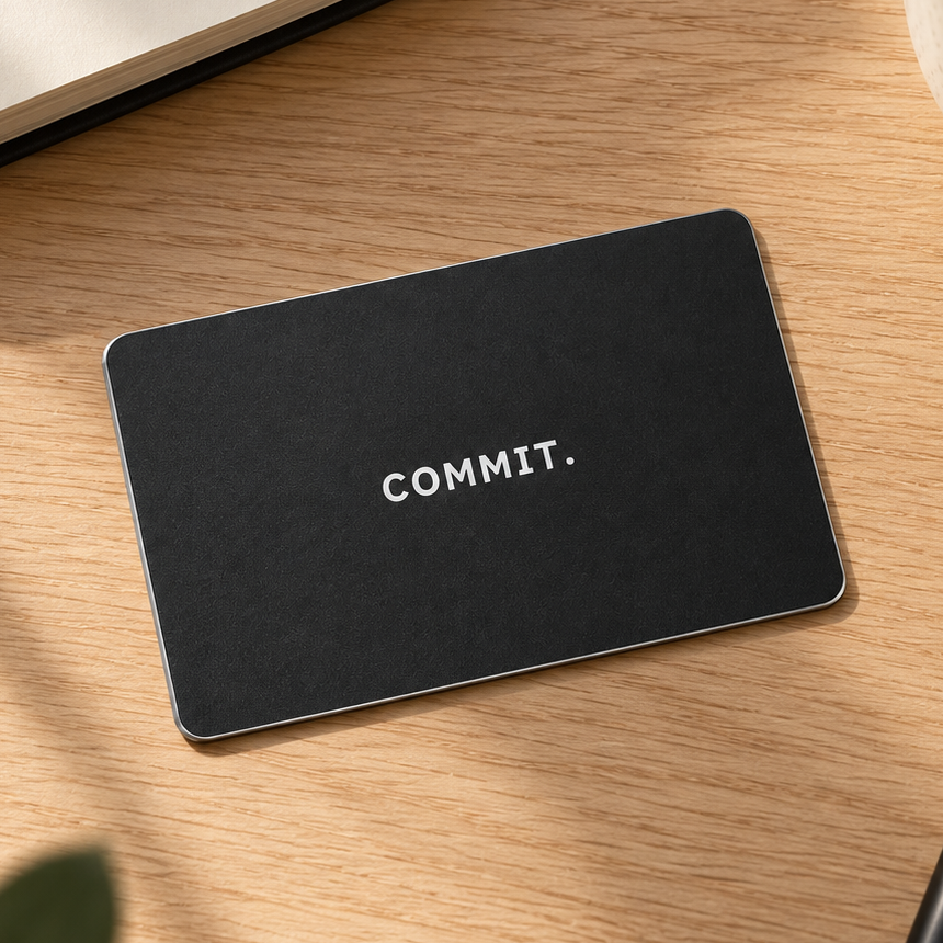 Black Commit Card on a wooden desk beside a notebook